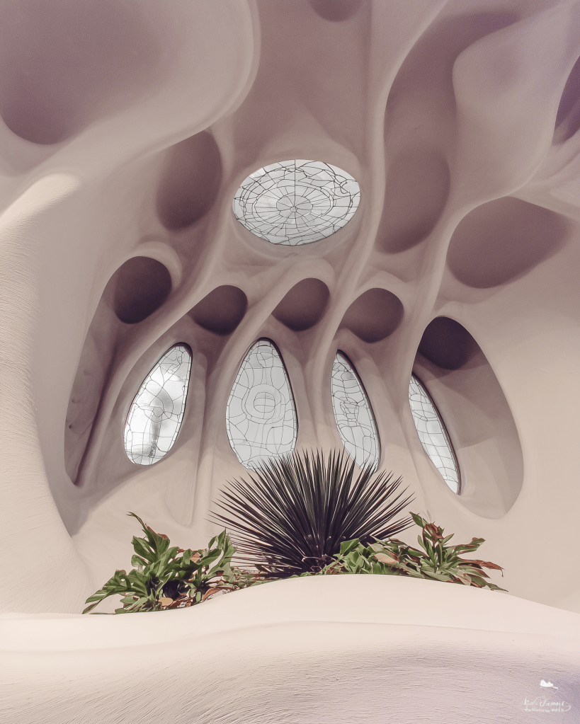 Interior view of a modern architectural space featuring organic shapes, large arched windows with decorative glass, and potted plants.